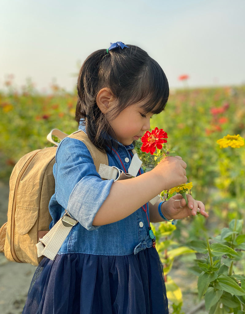 Asian toddler girl playing with flowers while wearing the Duck Duck Backpack